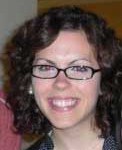 Carissa, who has brown curly hair and glasses, is smiling for a close-up headshot.
